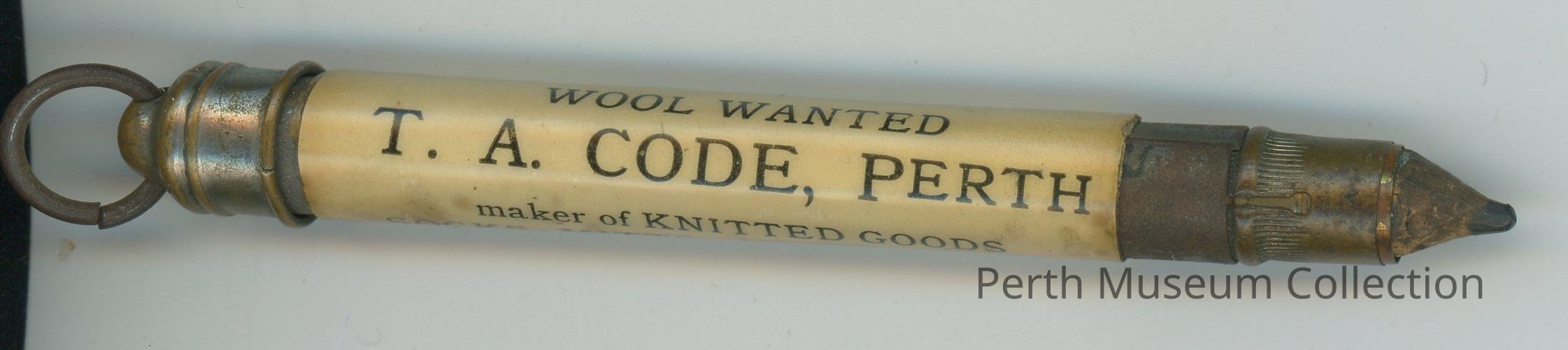 Pencil 1a - T.A. Code: The image shows an old brass bullet pencil with a ring at one end and a sharpened pencil tip at the other, featuring an advertisement on a paper label for "T. A. Code, Perth," a maker of knitted goods, with the phrase "Wool Wanted" indicating their business interest, suggesting the item likely served both as a writing tool and a promotional gift, typically used in a bygone era to advertise and spread awareness for local businesses in a practical manner.