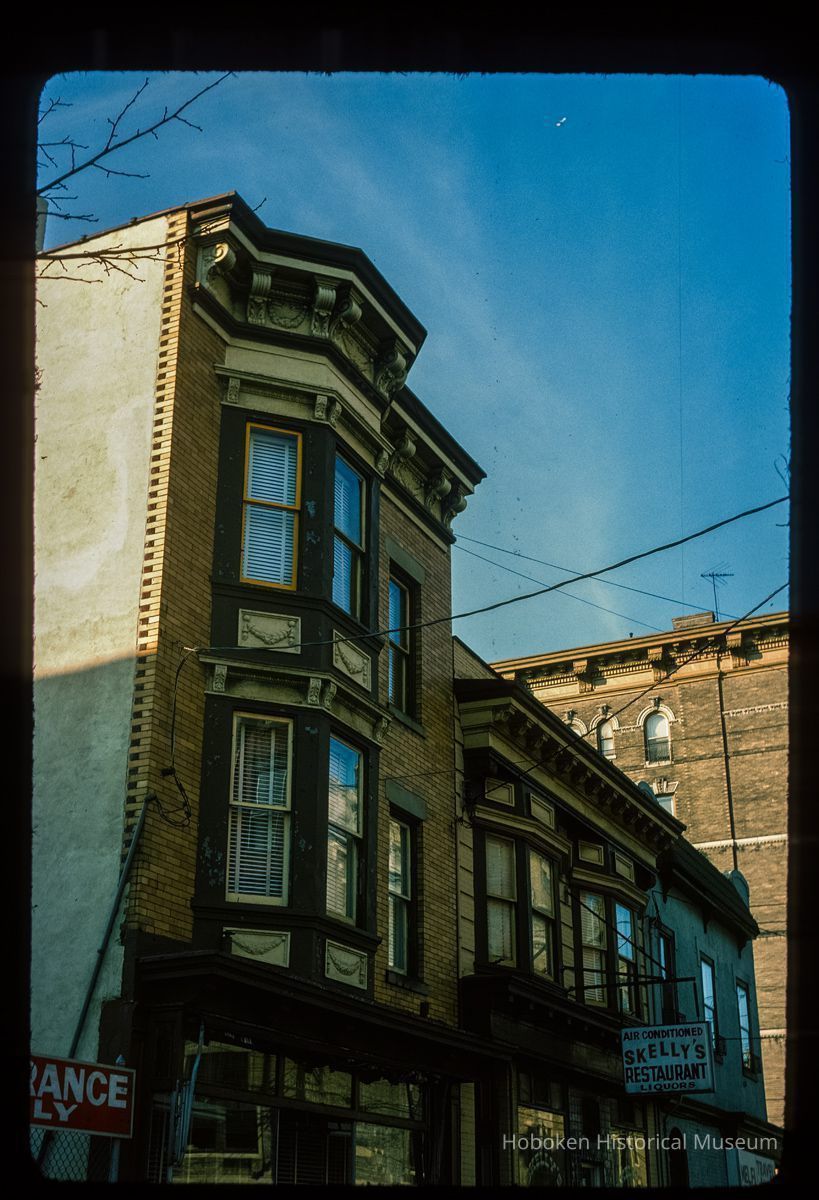 Color slide of close-up view of row house façades, cornices, brackets and bay windows including storefront signage reading 
