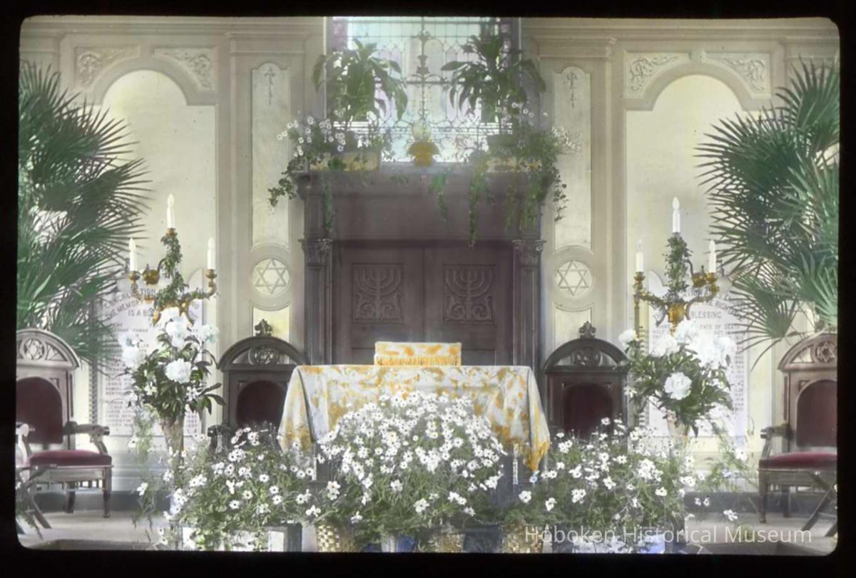 Lantern slide, color, of a synagogue interior with floral decorations, used for promotional display in Hoboken, no date, ca. 1920. picture number 1