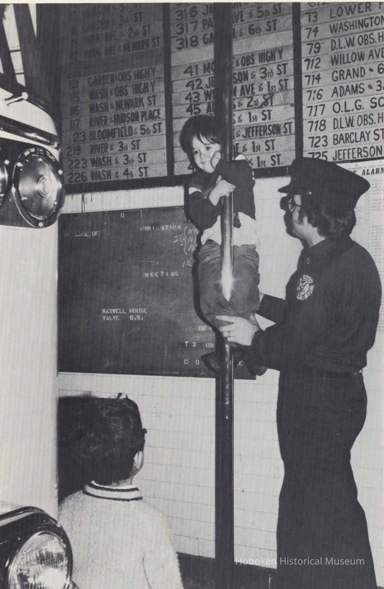 child sliding on fire pole; firemen; alarm board