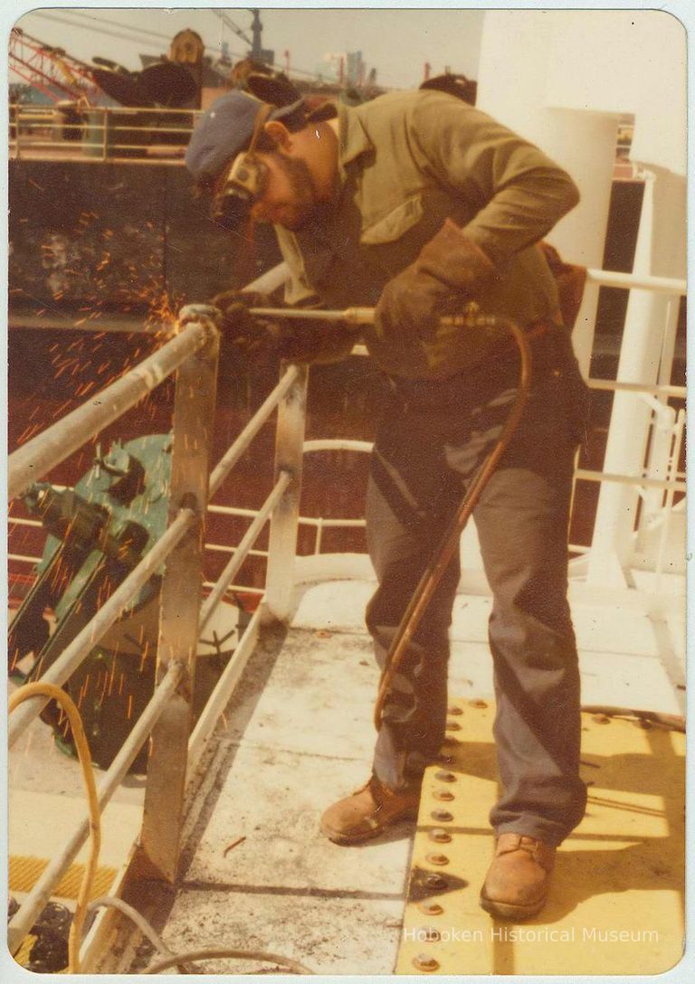 Color photo of Luis Denis using a torch on a ship railing at the Bethlehem Steel Shipyard, Hoboken Division, no date, ca. 1980. picture number 1