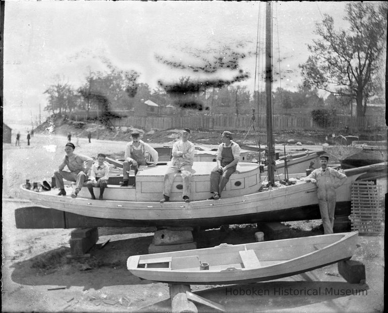 men and boats on riverfront near New Jersey Yacht Club clubhouse.