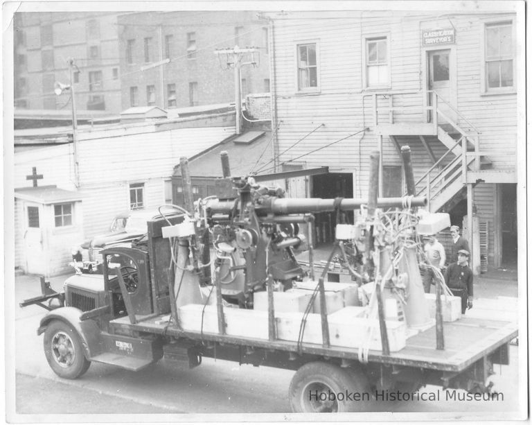 B+W photo of an artillery gun loaded on a truck below Classification Surveyor's office, Hoboken, no date, ca. 1942-45. picture number 1