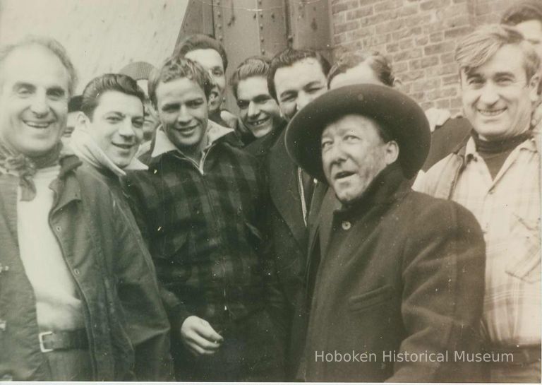 third from left: Marlon Brando; character actors and extras on pier