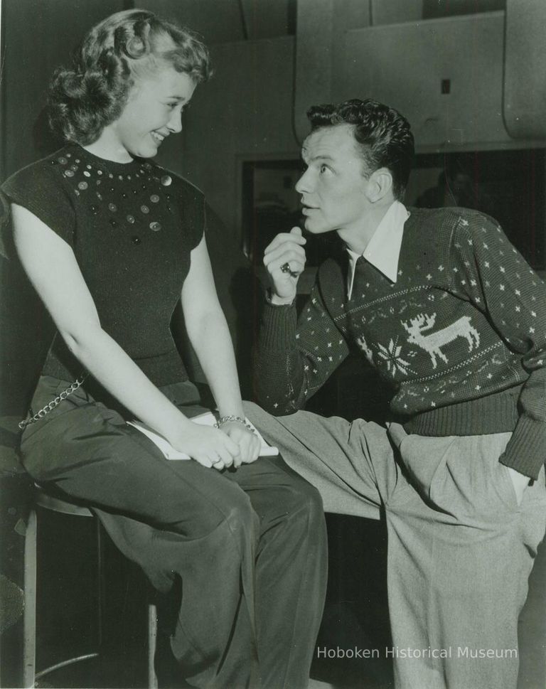 Black-and-white photo of Frank Sinatra, reindeer sweater, & Jane Powell in a posed radio studio 'candid' publicity shot, N.Y., no date, ca. 1946-47. picture number 1