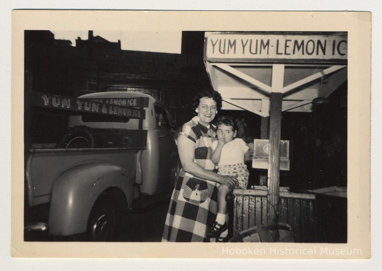 Digital image of b+w photo of a Aunt Rose holding a young child near a Yum Yum cart with truck, 416 Clinton St., Hoboken, n.d., ca. 1950s. picture number 1