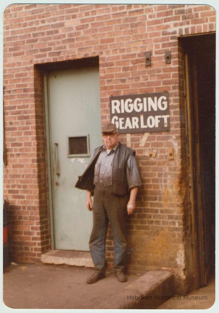 Color photo of Charlie Kosbab standing under the sign, Rigging Gear Loft,at the Bethlehem Steel Shipyard, Hoboken Division, ca. 1980. picture number 1