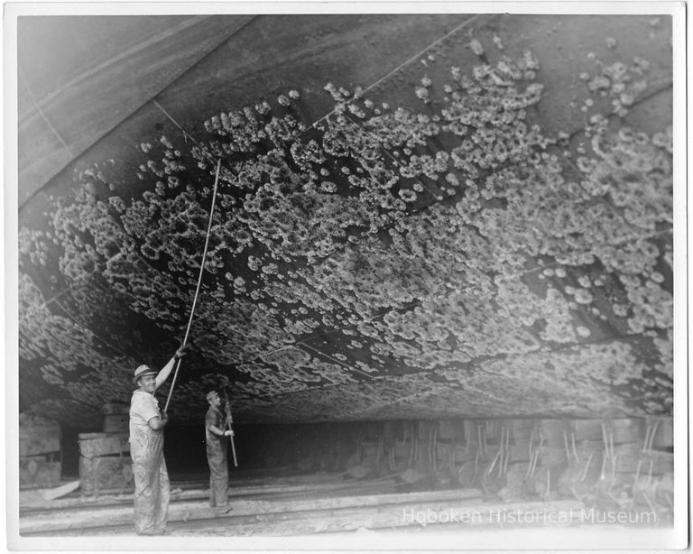 B+W photo of 2 workers scraping hull of unknown ship in drydock, Hoboken, no date, ca. 1940. picture number 1