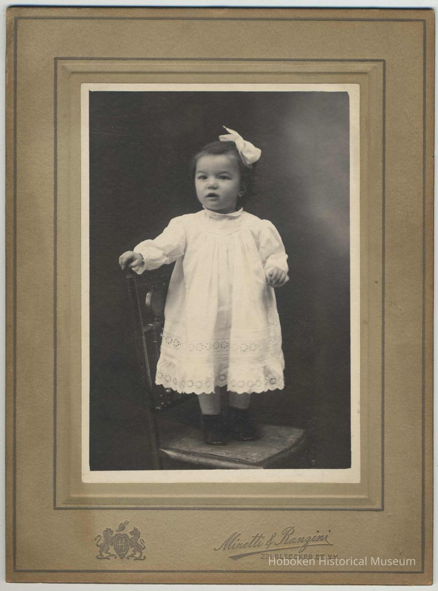 Sepia-tone photo of an unidentified baby, ca. 1-2 years old, posed standing on a chair in a studio, New York City, no date, ca. 1900-1910. picture number 1