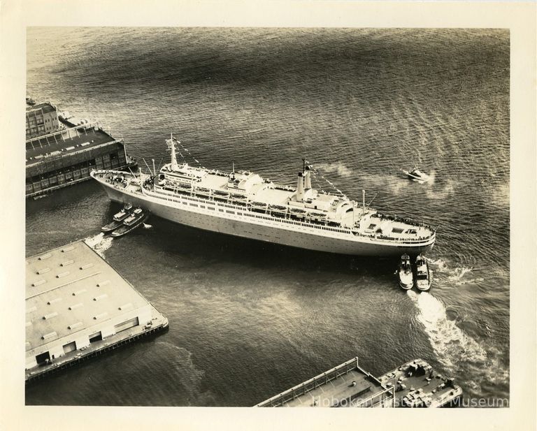 image: S.S. Rotterdam being moved by tugboats to Hoboken pier 5