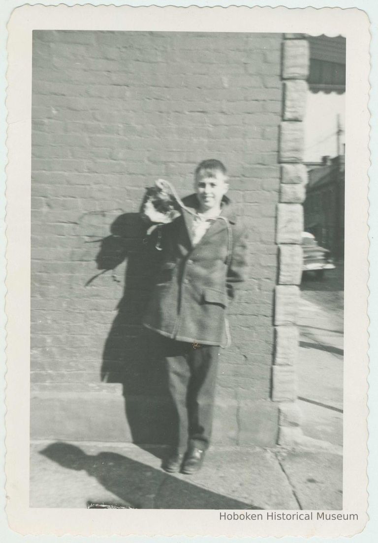 B+W photo of a boy(?) leaning against a wall & holding a doll on Clinton Street near Willow Terrace, Hoboken, [1959]. picture number 1