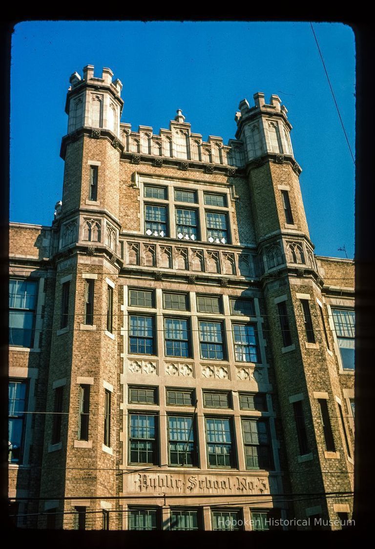 Color slide of close-up view of façade, brick turrets, parapet, and frieze reading 