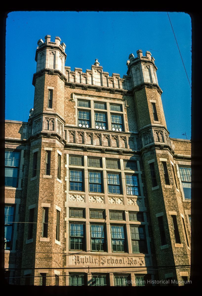 Color slide of close-up view of façade, brick turrets, parapet, and frieze reading 