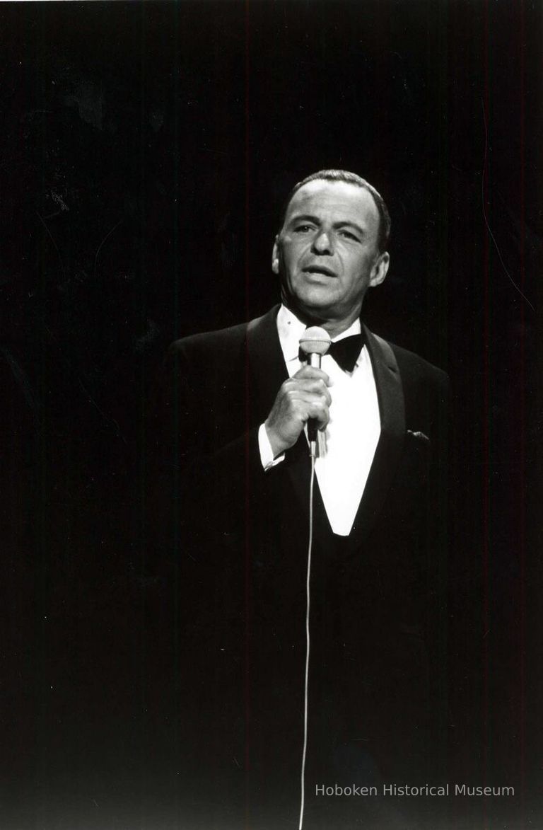 older Frank Sinatra in concert, holding microphone