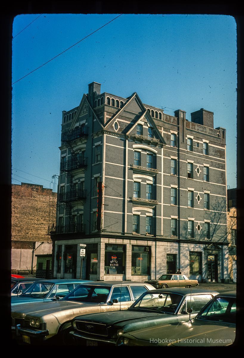 Color slide of eye-level view of front and side façades with fire escape at 77 Hudson Street on the NE corner of Hudson Place occupied by the Victor Hotel picture number 1