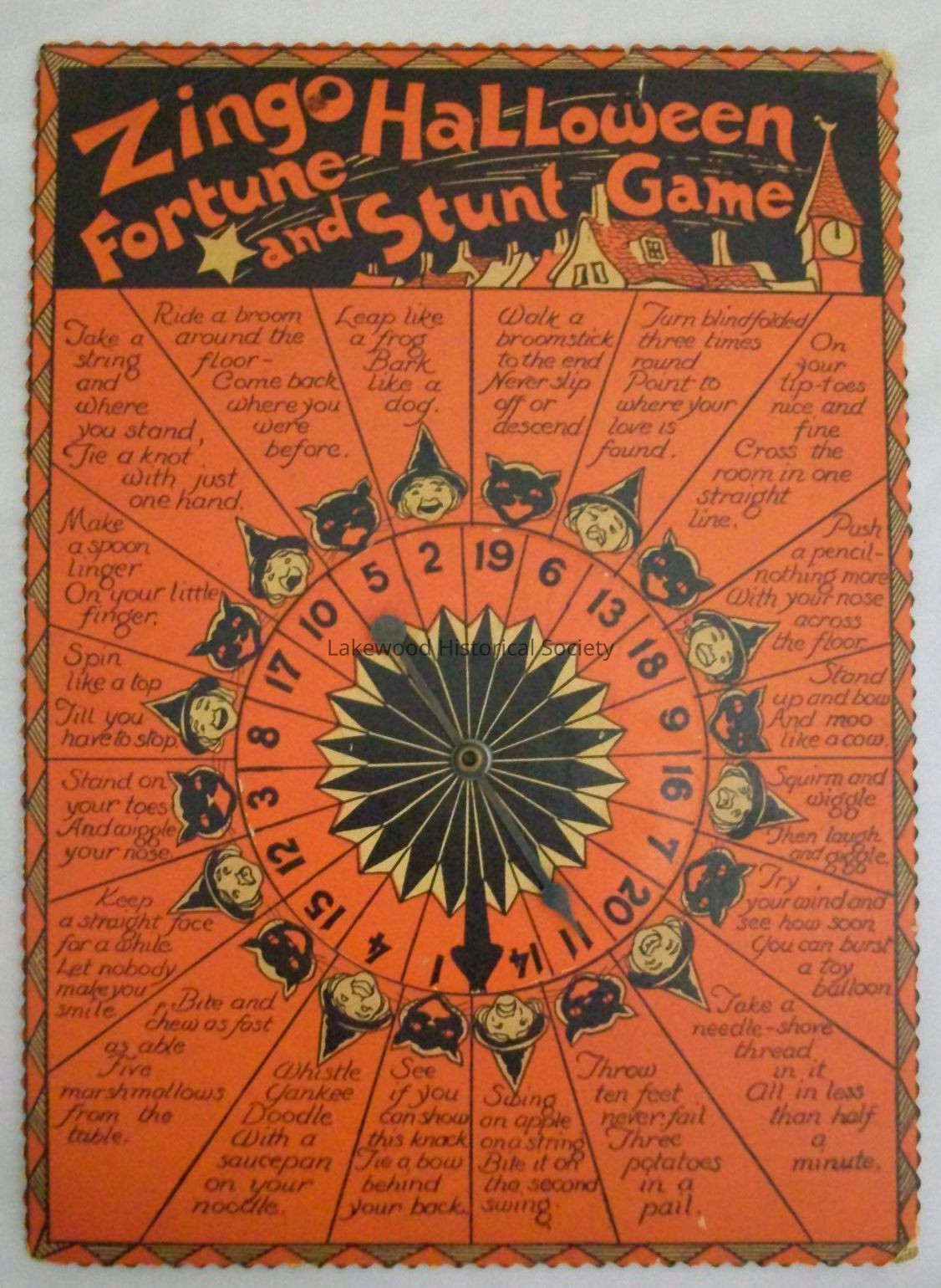 Front: The front of the game board. The game is primarily a bright orange, with black and slightly yellowed ink creating various images. At the top of the game is a section with roofs of a town and the words "Zingo Halloween Fortune and Stunt Game" in bright orange letters at the top. Beneath is the body of the game, where there is a spinner divided into 20 sections. Each section has either a witch or a cat. The spinner is in the middle. There are different tasks in each of the sections.