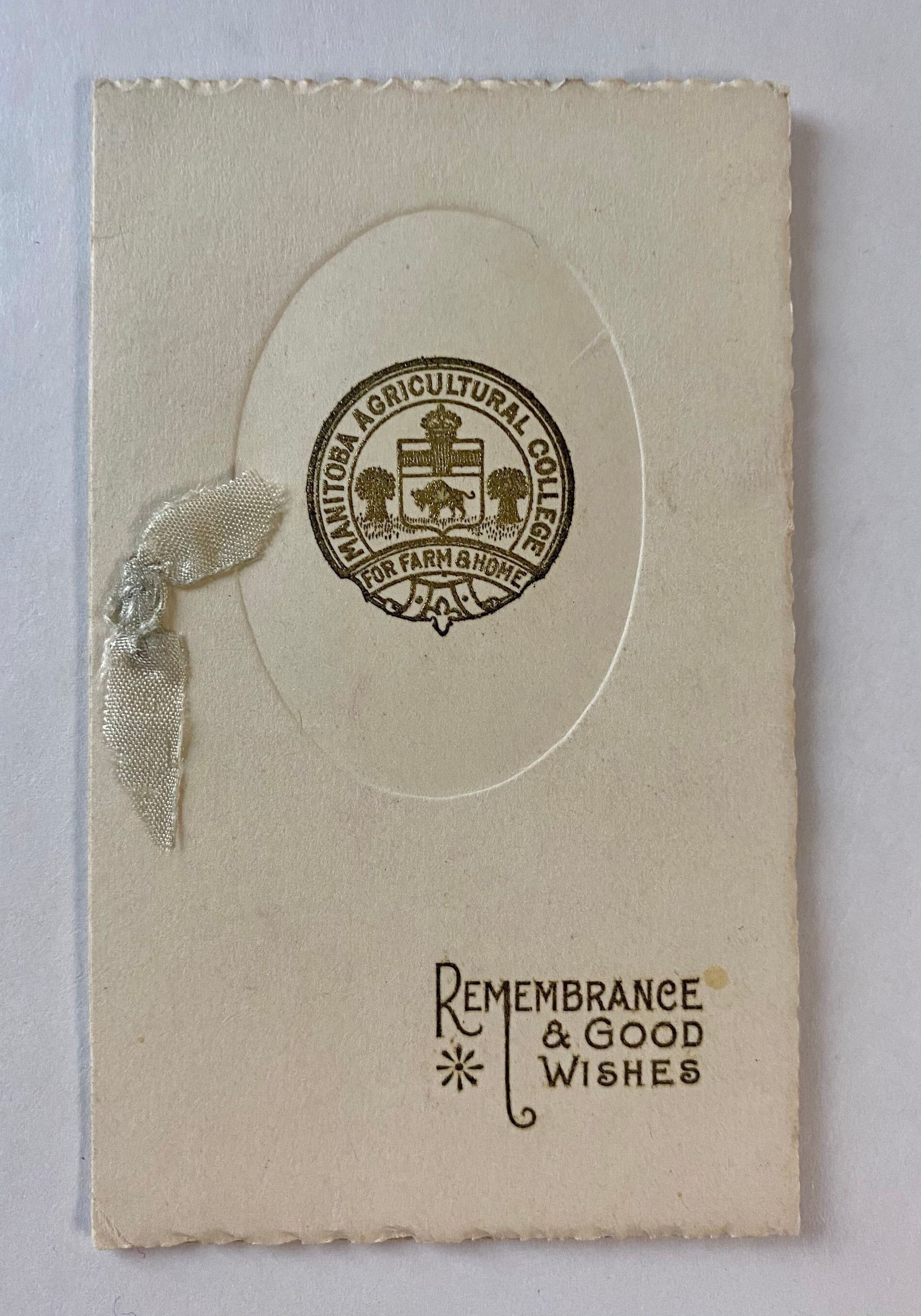 The image shows an elegant, vintage card featuring a gold-embossed emblem of the Manitoba Agricultural College with the words "FOR FARM & HOME" and a decorative ribbon attached on the left; below the emblem, the card bears the inscription "REMEMBRANCE & GOOD WISHES" in a stylish font, suggesting it may have been used for personal correspondence or as a commemorative keepsake, highlighting its historical and sentimental value, while also reflecting a sense of nostalgia and formal elegance.