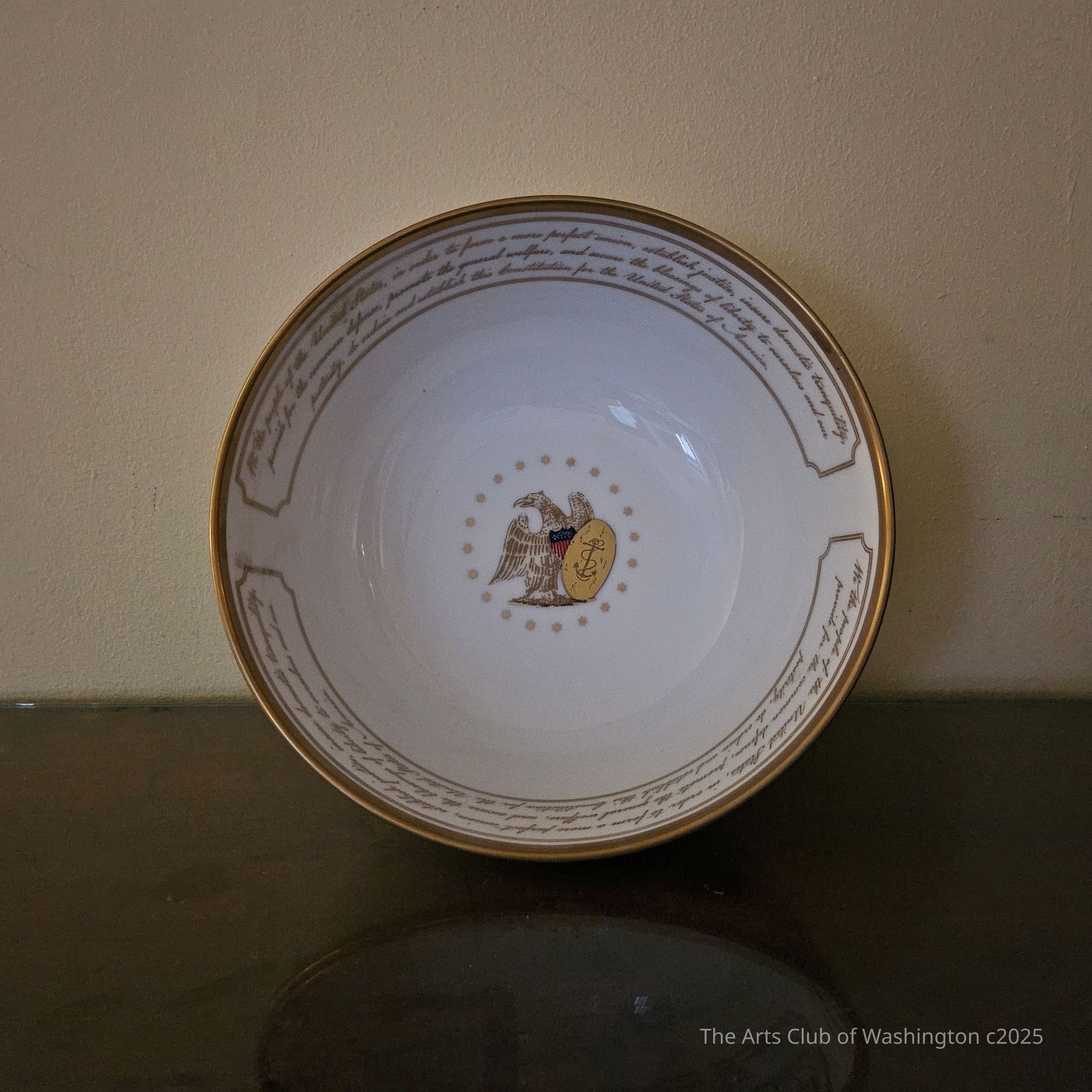Bowl, Woodmere China Inc., porcelain, ca. 2000-12.: Porcelain bowl, decorated with a gold edge, surrounding an inscription in script (see inscriptions tab). Centered in the well of the plate is an American Eagle with a shield of stars and stripes and a gold oval decorated with a rope entwined anchor, surrounded by 20 gold stars.