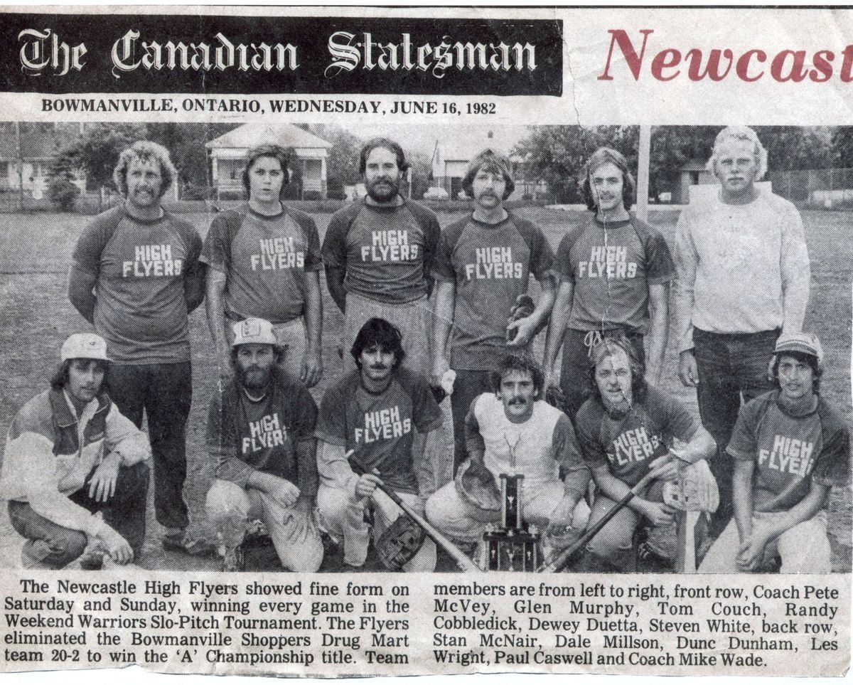 Newcastle High Flyers Baseball Team (Statesman News Article Clipping): This black and white newspaper clipping is from "The Canadian Statesman" dated June 16, 1982, although the word Newcastle is in red. A group of twelve young men, identified as the Newcastle High Flyers, are posing on a field, divided in two rows, six in the back are standing up, and the other six are crouching down in the front. They are all wearing matching T-shirts that read "HIGH FLYERS", although the sixth man on the right in the back row is wearing a longsleeve white shirt, and the first man on the left in the front row is wearing a jacket. The team appears to be celebrating a victory, as the text below emphasizes their success in the Weekend Warriors Slo-Pitch Tournament, where they won the ‘A’ Championship title.