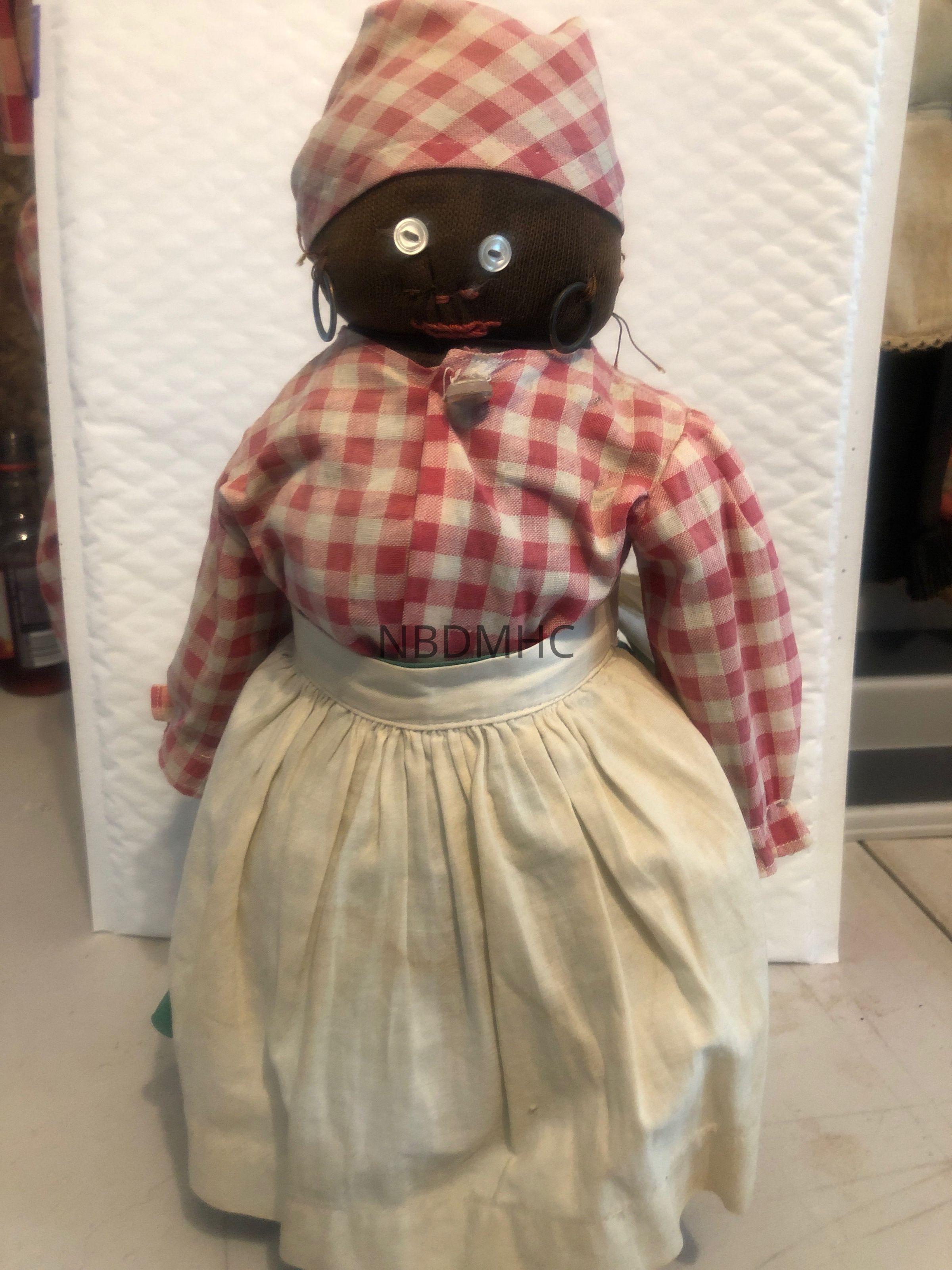 This 12" chubby bottle doll is a charming and unique addition to any doll collection. With her hoop earrings and button-eyed embroidered nose and mouth, she exudes a sense of playful elegance. Her vibrant red and white shirt perfectly complements her solid green skirt, creating a delightful contrast of colors. To complete her ensemble, she wears a checkered headscarf that adds a touch of vintage charm. This doll is meticulously crafted with attention to detail, making her a true work of art. Whether displayed on a shelf or used for imaginative play, this bottle doll is sure to capture the hearts of doll enthusiasts of all ages.