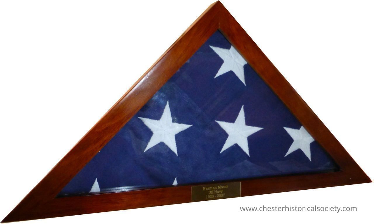 Herman Moser's USA Flag Memorial in display case.: The image depicts a neatly folded American flag encased in a triangular wooden display box, featuring several white stars on a blue background; beneath the glass, there is a plaque inscribed, "Herman Moser US Navy 1920 - 2007," commemorating Herman Moser's WWII service in the
US Navy, signifying honor and remembrance.