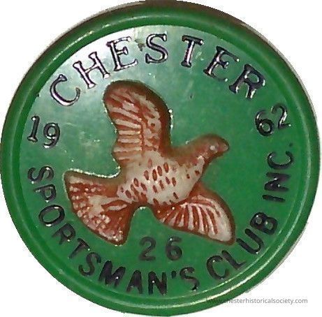 1962 Chester Sportsmen Club pin #26: The image shows a circular plastic green badge featuring an embossed design at its center of a brown bird in flight, surrounded by the text "CHESTER SPORTSMAN'S CLUB INC" in uppercase letters arching around the top and bottom edges, with the numbers "1962" split on either side of the bird, suggesting a date, and the number "26" positioned at the bottom center beneath the bird, possibly indicating a membership or identification number.