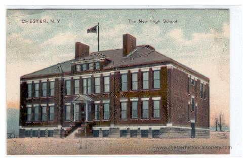 Chester, N.Y. The New High School: The image depicts a postcard featuring "The New High School" in Chester, N.Y., showing a substantial two-story brick building adorned with numerous windows and American flags proudly flying on a rooftop flagpole, set against a serene sky with handwritten inscriptions at the bottom.
