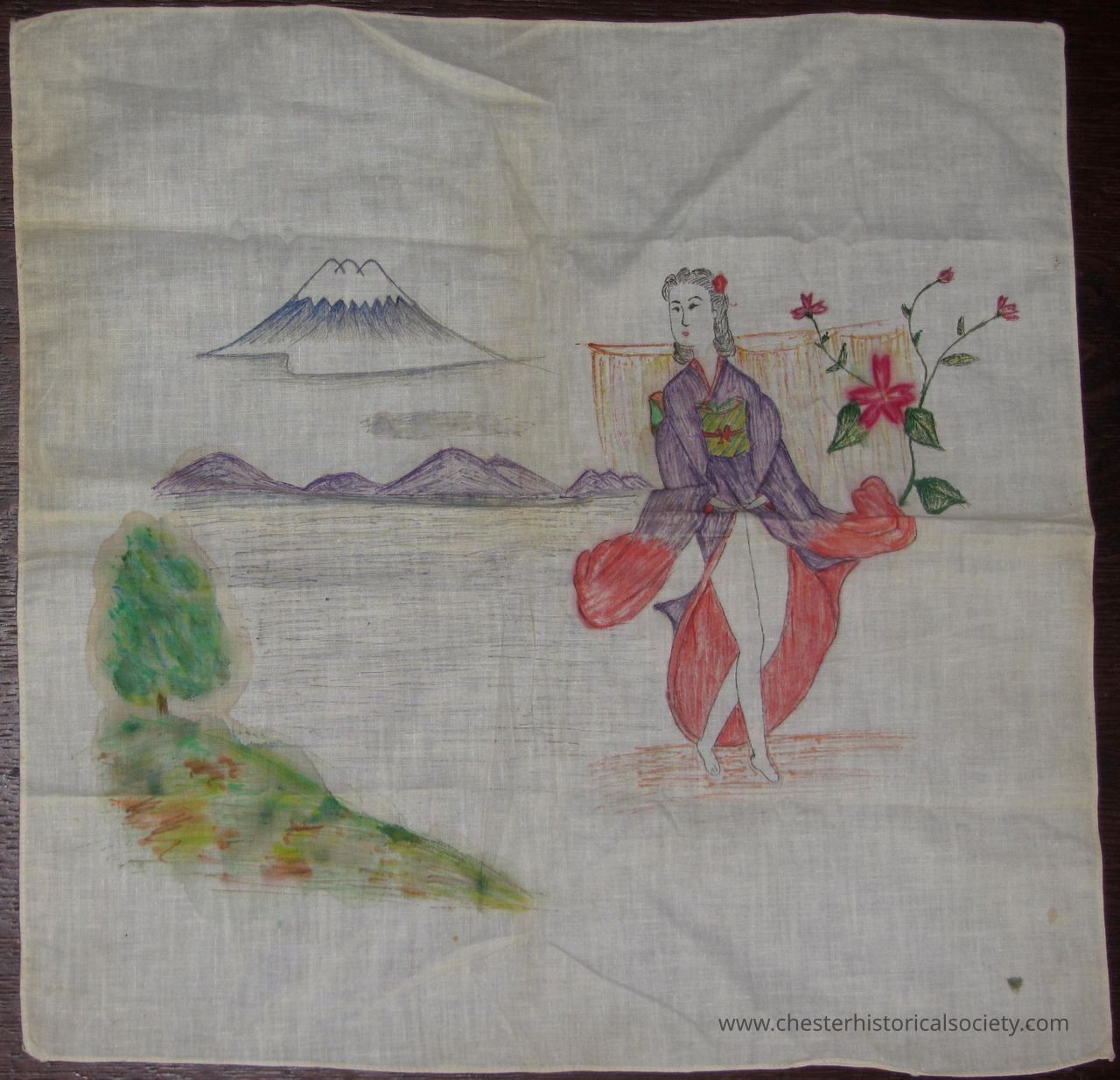 John J. McGrath's Souvenir Hankie (Geisha): The image depicts a hand-drawn scene on fabric, featuring a person dressed in traditional Japanese attire, possibly a kimono, adorned with vibrant colors like purple and red, standing elegantly beside a flowering plant with pink blossoms. In the background, there is a serene landscape with a snow-capped mountain, most likely resembling Mount Fuji, and a range of low hills or distant mountains. Below this picturesque setting, there is a soft depiction of greenery that seems to represent a grassy or vegetated area, adding