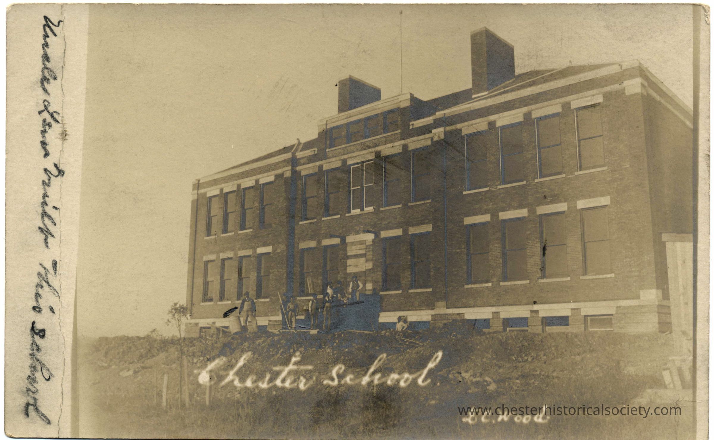 Chester School: This monochrome photo postcard captures the 1906 two-story brick school building under construction, identified as "Chester School" by the handwritten inscription on the bottom. Several workmen are in front of the building's main entrance. The architecture features prominent window structures and brickwork, characterized by an early 20th-century American design, complemented by minimal landscaping and an overcast sky. The photograph, faded and aged, retains a nostalgic memory of educational history.