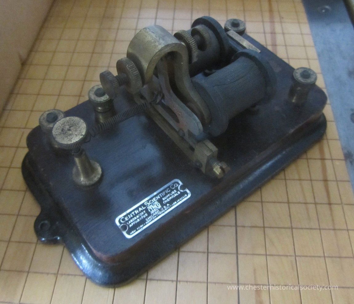 Telegraph Relay Central Scientific: The image depicts an antique telegraph machine, which features a sturdy, dark-colored wooden base with metal components including screws, terminals, and a coil, suggesting its use in early communication technology. The device is likely to have been used for sending Morse code messages, indicative of the era before modern digital communication. Its craftsmanship and materiality reflect the industrial design of historical scientific instruments. A metal plate on the base details the manufacturer's specifics.