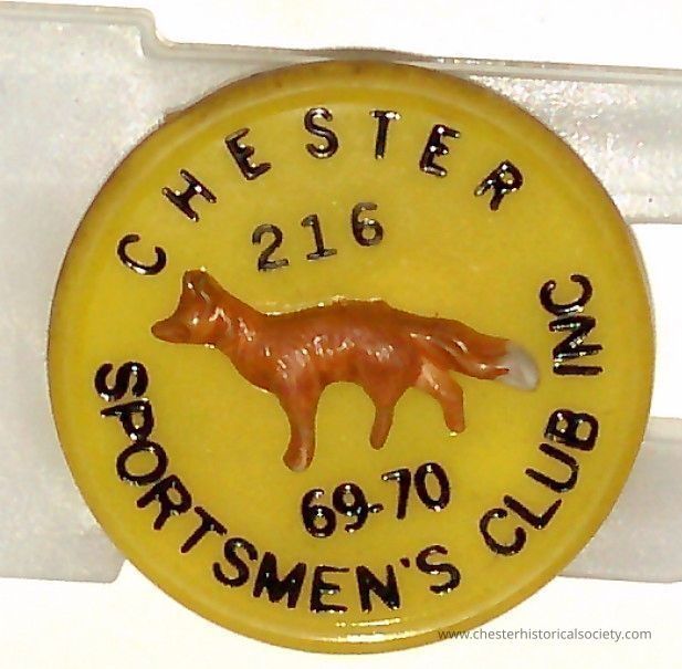 Chester Sportsmen Club 1969-70 pin #216: This image features a round yellow plastic badge with the illustration of a brown fox in the center, surrounded by the text "CHESTER SPORTSMEN'S CLUB INC 69-70" around the edge, indicating membership number "216" or affiliation with a sportsmen's club during the 1969-1970 period.