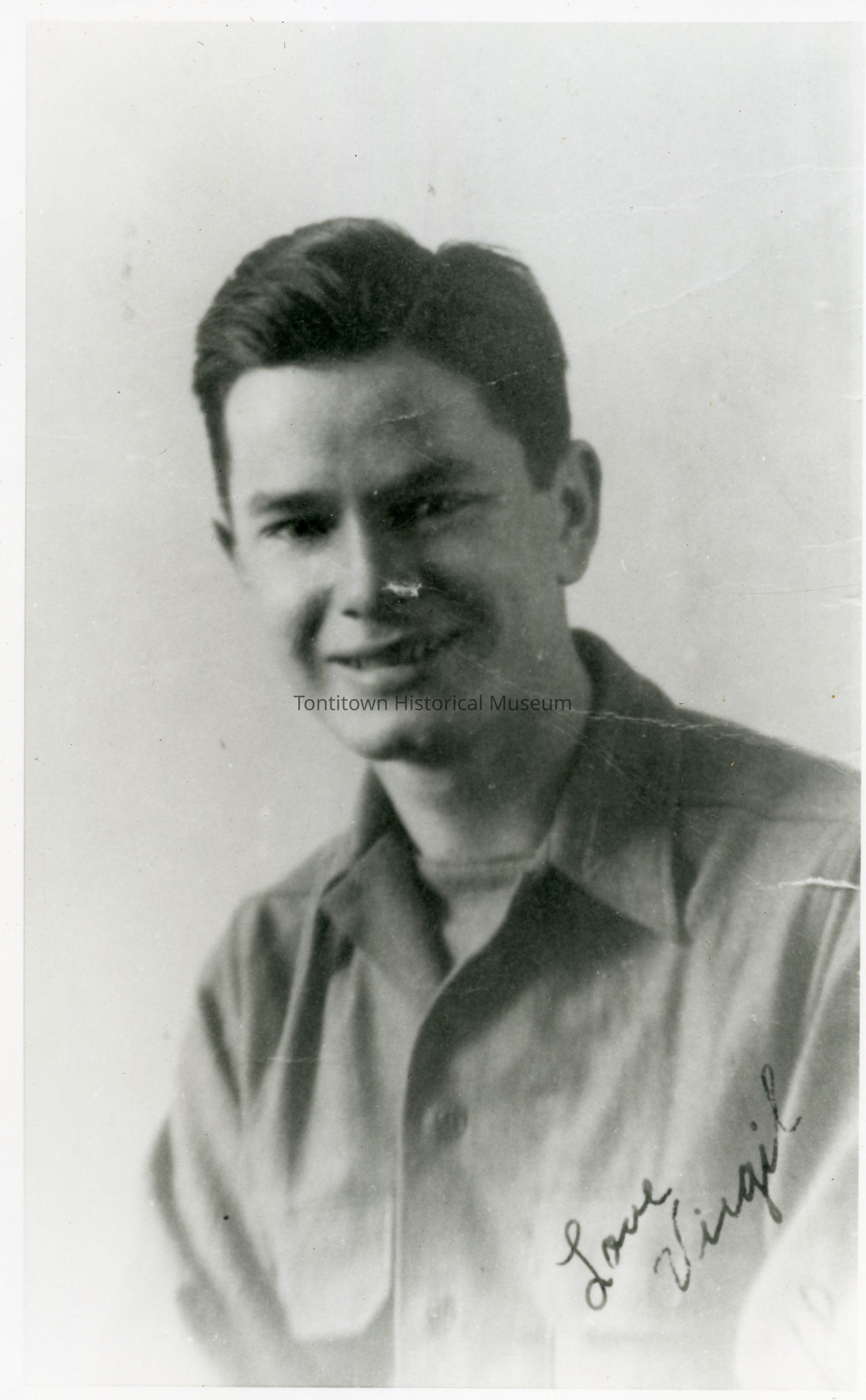 The image is a black and white portrait of a smiling man with short, neatly combed hair, wearing a button-up shirt with a subtle shine to its texture, captured against a plain backdrop; his expression exudes warmth and friendliness, while the bottom of the photograph features a handwritten inscription that reads "Love Virgil," suggesting a personal touch, possibly indicating a cherished memory or affectionate message intended for someone special, encapsulated within the timeless quality of this classical portrait style, enhancing its sense of nostalgia and