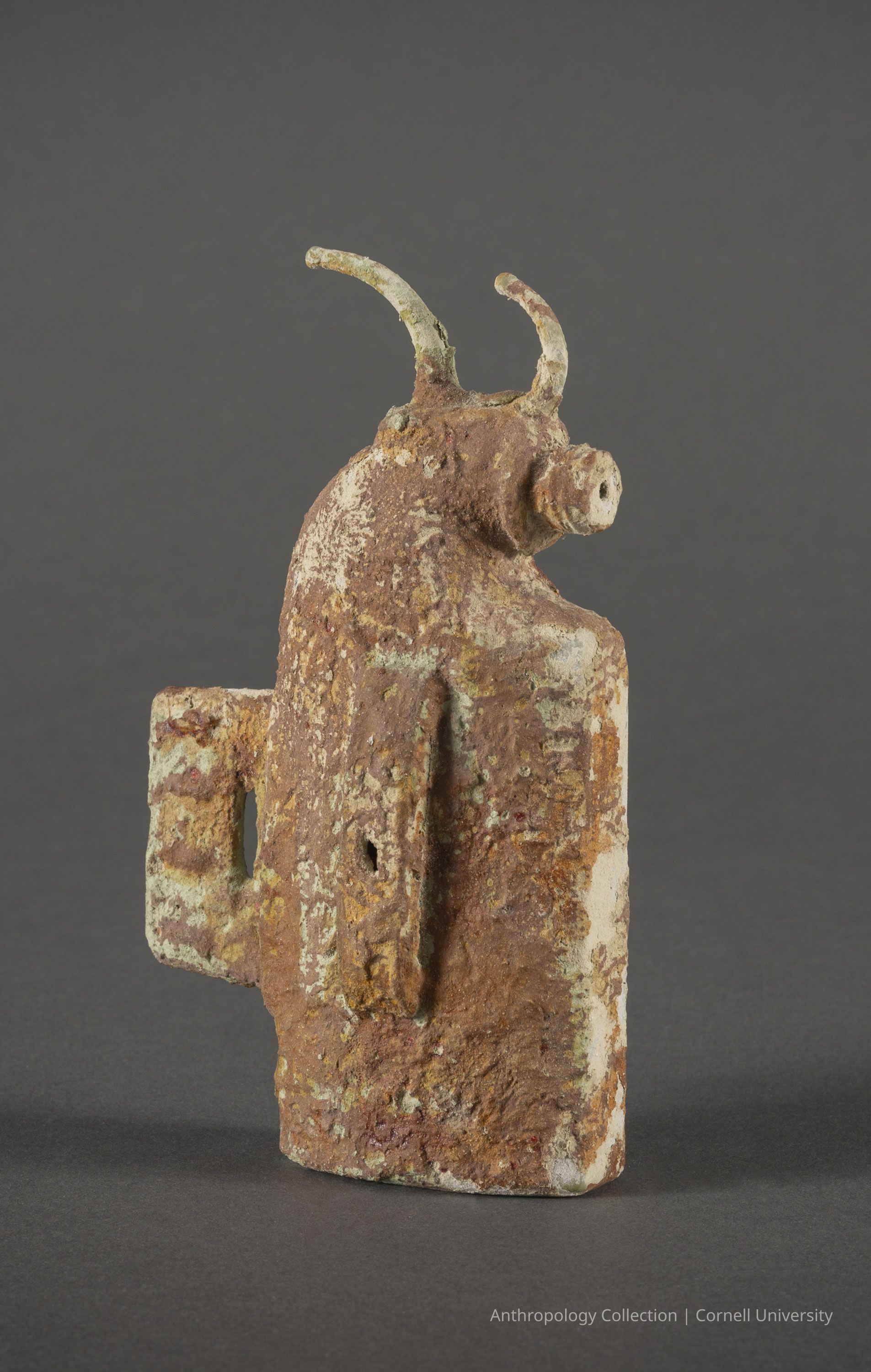 MIETHYMIATERION (Candelabra-vaporizer-incense burner) | circa 1966-71 | Photo by Ann Cady, 2024 | ©2026 Norman Daly Art: The photo shows a weathered, ancient Llhuroscian artifact characterized by its rough, rusted surface and patina that suggests age and exposure to the elements over time; it resembles a stylized bull with prominent curved horns and a simplistic form, indicative of early artistic expression, from the archaic civilization. It captures both the strength and cultural significance of the animal in its time, while the muted hues of brown and green reveal its antiquity, creating an evocative representation of historical artistry.