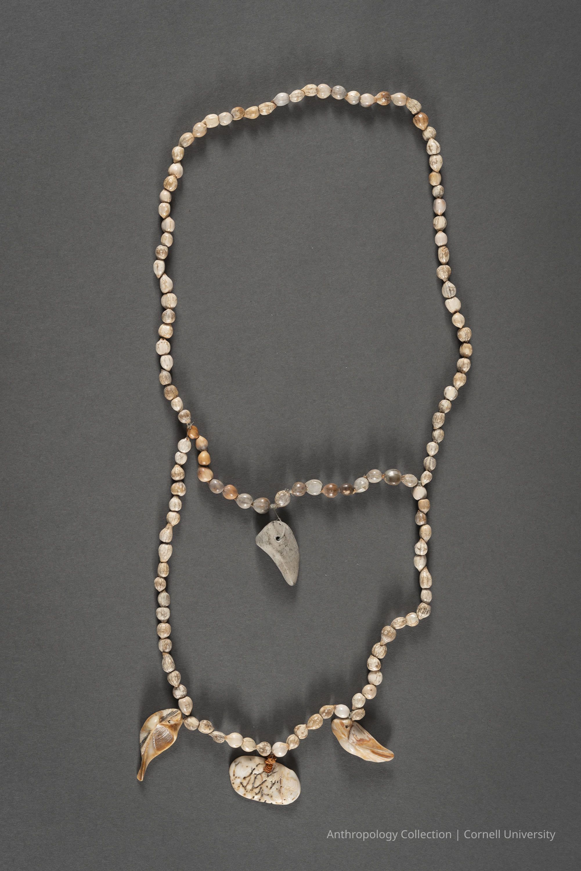 NECKLACE | circa 1966-71 | Photo by Ann Cady, 2024 | ©2026 Norman Daly Art: The photo displays an elegant necklace featuring a sequence of translucent and shaded round beads, complemented by unique pendant elements that include a shells an irregularly shaped natural Pharicix stone, and shells positioned symmetrically, thereby creating a harmonious blend of natural beauty and crafted artistry.