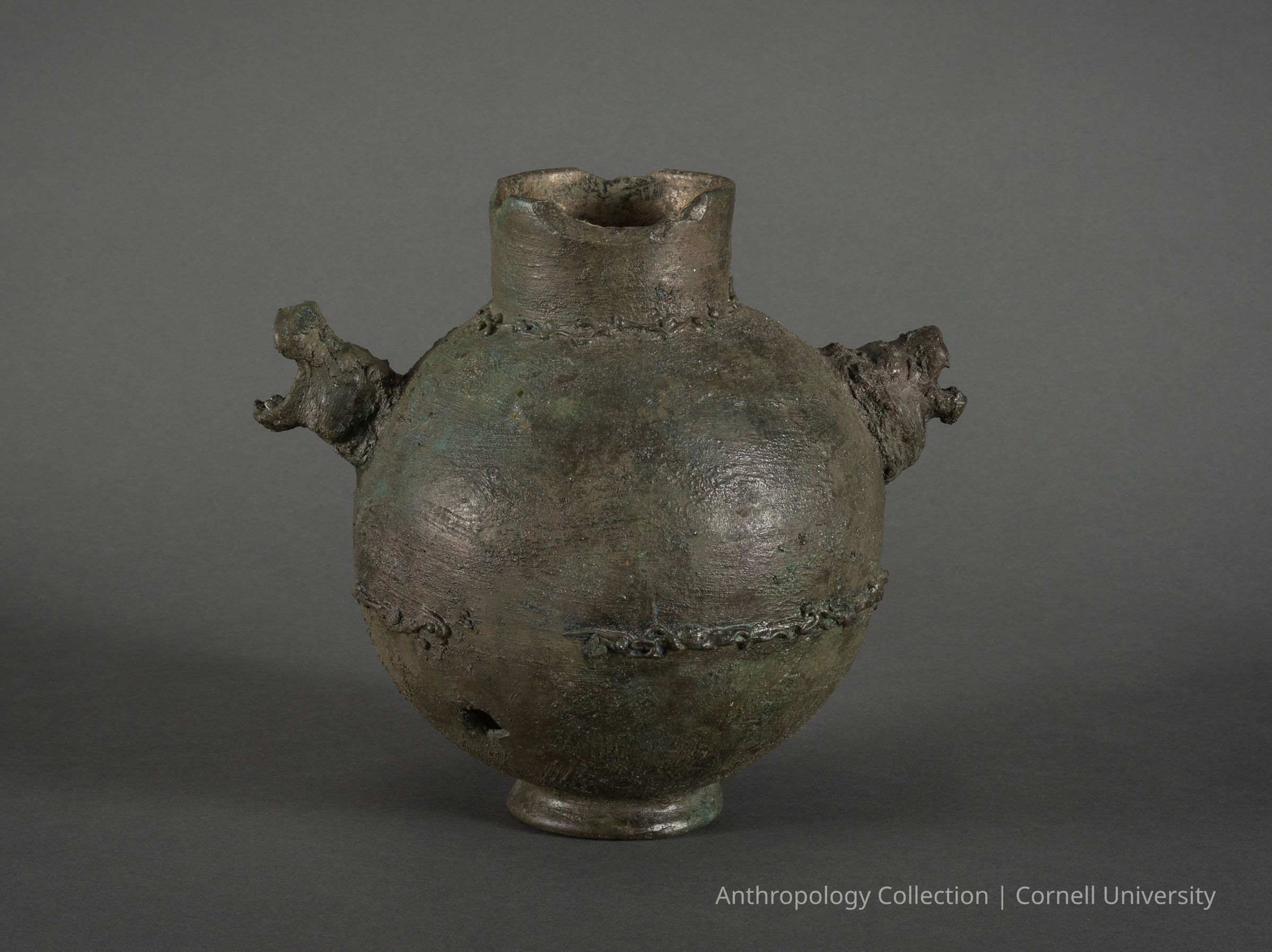ESNONTOS (Urn) | circa 1966-71 | Photo by Ann Cady, 2024 | ©2026 Norman Daly Art: This image displays an ancient, dark bronze vessel with a large, round body and two protruding handles on either side, resembling animal heads (hippo and lion) Its rough, textured surface and craftsmanship, suggesting historical significance or ceremonial use, possibly in rituals or as a utilitarian item.