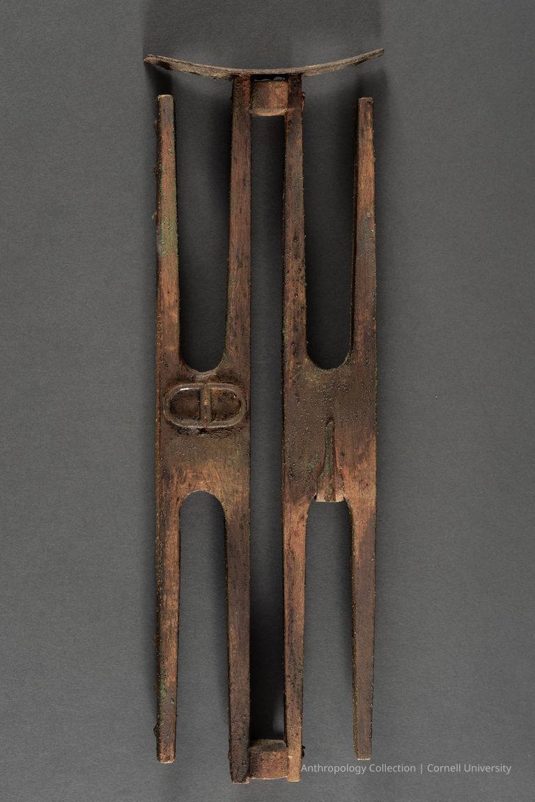 A PAIR OF STILT-WALKERS (Devout Couple) | circa 1966-71 | Photo by Ann Cady, 2024 | ©2026 Norman Daly Art — The image displays an ancient, weathered artifact crafted primarily from wood, featuring two slightly different vertical pieces joined at the top with a carved piece joining the top of each.
