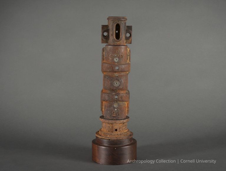 VOTIVE FIGURE | 1965 | Photo by Ann Cady, 2024 | ©2026 Norman Daly Art — This intriguing cylindrical object consists of stacked, rusted metal parts, each marked with numbers and letters, creating a columnar form. It is mounted on a dark, circular wood base. Each component showcases wear and oxidation, which enhances the texture and enriches the visual impact of figure, suggesting esting themes of decay, history, and transformation.