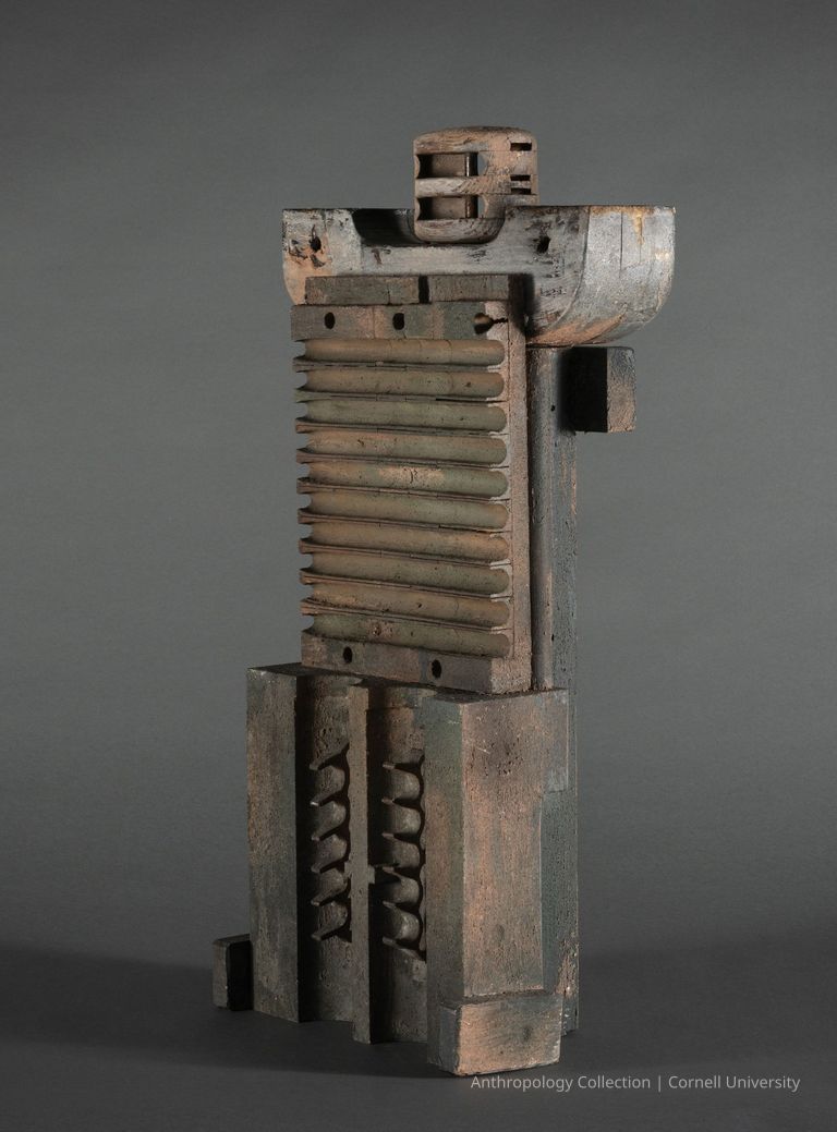 EARLY VOTIVE OF SHOR-NOO | circa 1966-1971 | Photo by Ann Cady, 2024 | ©2025 Norman Daly Art — The photo displays a religious artifact that eerily resembles machine parts. It is composed of wood and primarily of oxidized metal parts including a vertically ribbed wood section, notched elements, and various angular forms, revealing an ancient aesthetic offering a visually intriguing exploration of material and form.