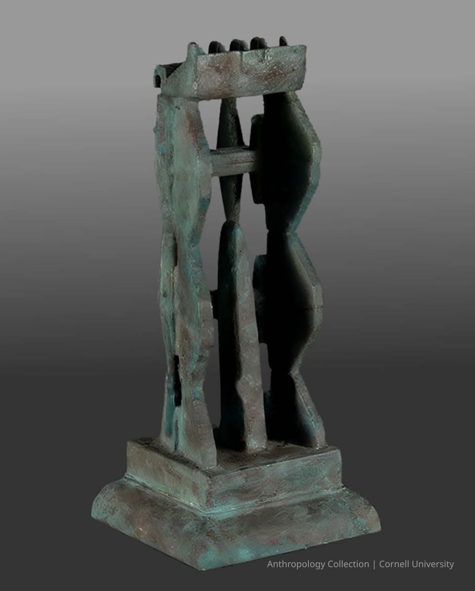 MINIATURE VERSION OF A PRIE-DIEU | 1966-71 | Photo by Ann Cady, 2024 | ©2026 Norman Daly Art: A metallic artifact, possibly made of bronze or copper, with a greenish patina indicative of age and oxidation, featuring a sturdy rectangular base and an intricate structure rising vertically with a central axis, flanked by symmetrical, textured elements on either side; atop the structure are small, evenly spaced pointed projections arranged in a row, suggesting a function or symbolic purpose.