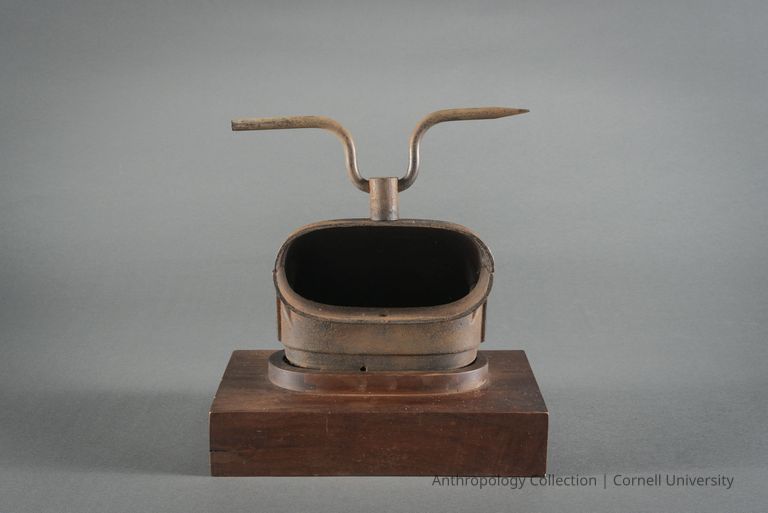 Alternative view of VOTIVE FIGURE | circa 1965 | Photo by Ann Cady, 2024 | ©2026 Norman Daly Art — The image shows a votive resembling a rusted metallic helmet with an open visor mounted on a wooden base; attached to the top is a bent metal rod that forms horns or antennae, portraying an abstract and intriguing artifact.