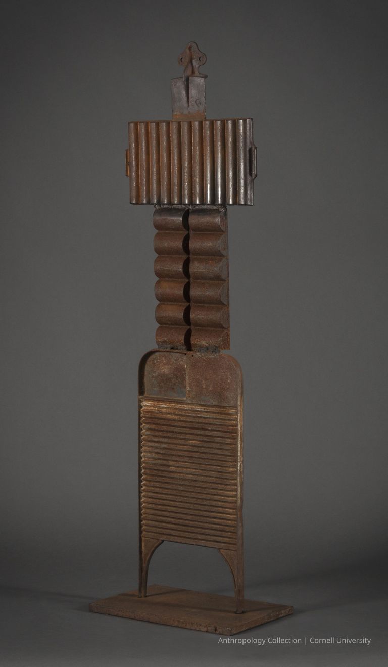 VOTIVE | circa 1961-65 | Photo by Ann Cady, 2024 | ©2026 Norman Daly Art — This striking rusty metal figure is comprised of three rectangular pieces with vertical and horizontal ridges. Tthe 'head' topped with a pieces of small hardware and short 'legs' are attached to heavy iron base.