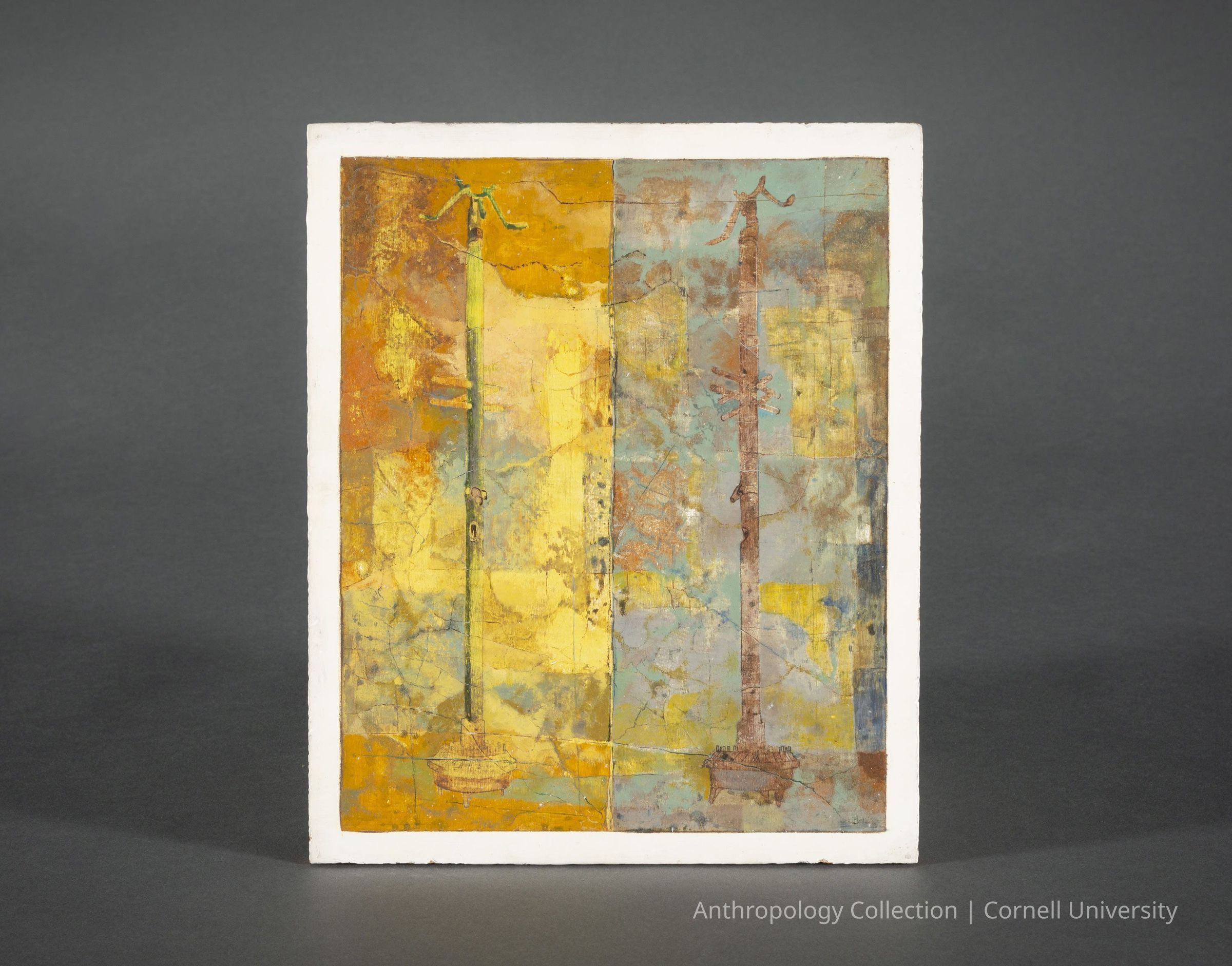 FACSIMILE OF WALL PAINTING FROM THE TEMPLE ON THE BAY OF ANSES | circa 1966-1971 | Photo by Ann Cady, 2024 | ©2026 Norman Daly Art: This facsimile of a temple wall painting features a textured, abstract painting divided into two distinct vertical sections, each dominated by earthy tones of yellow, brown, and muted blues. The left section has a yellowish hue with geometric patches, while the right displays a cooler, bluish tone. Each side depicts tall, slender, pole-like structure extending vertically, each adorned with branch-like extensions at the top. The facsimile is framed with a simple white border, enhancing the contrast between the vibrant colors and the dark gray background against which it is displayed.
