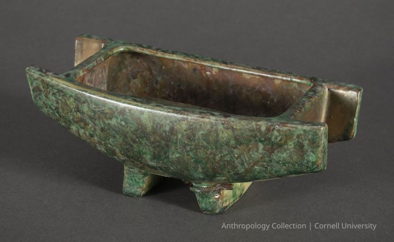 UNIDENTIFIED | circa 1966-71 | Photo by Ann Cady, 2024 | ©2026 Norman Daly Art — The photo features an ancient oblong bronze vessel with a verdigris patina, standing on four sturdy legs, characterized by its minimalist yet functional design, likely used in Llhuroscian ritualistic or ceremonial practices; its surface shows aging and use, reflecting its historical and archaeological significance.