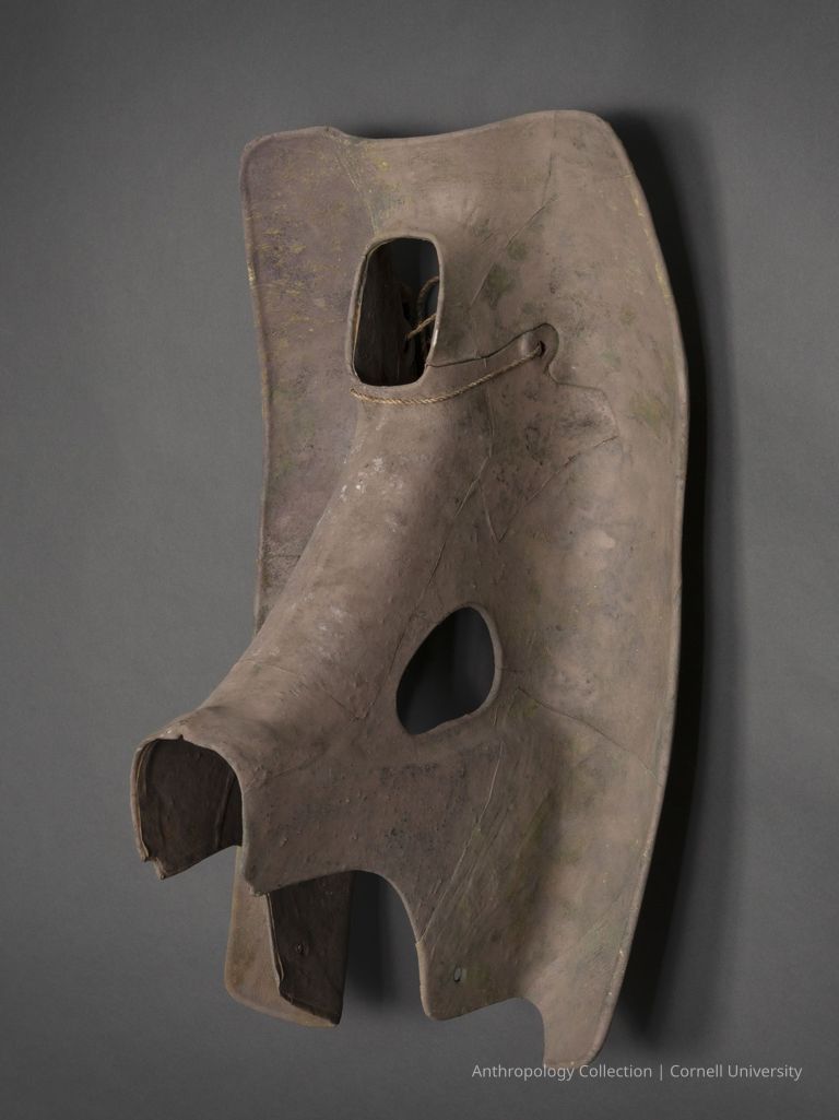 ELELEPHANT MASK | 1966-71 | photo by Ann Cady, 2024 | ©2026 Norman Daly Art — A weathered, brown object made from a natural material resembling bark or wood, featuring three distinct openings, elegantly suspended against a neutral, gray background.