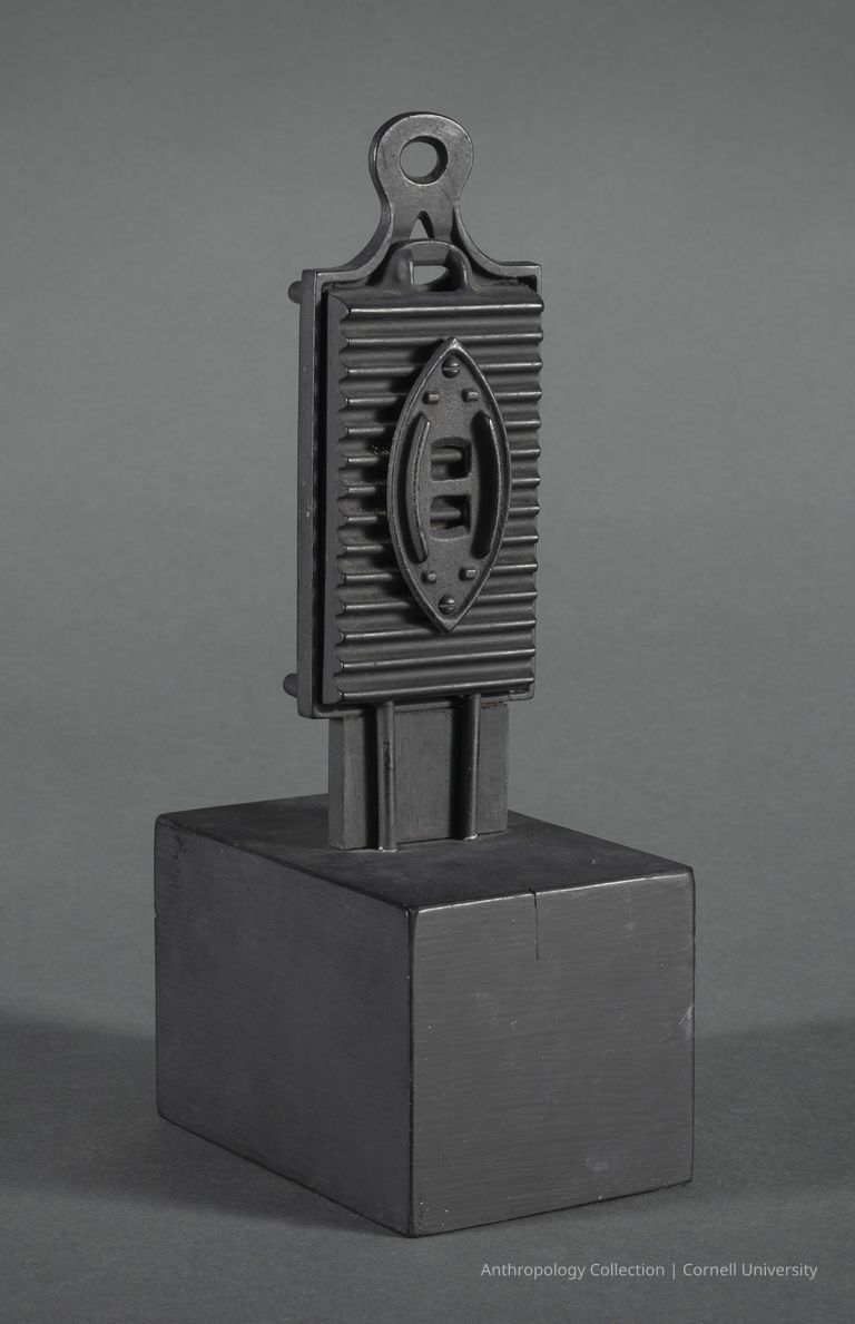 VOTIVE FORM | circa 1965-71 | Photo by Ann Cady, 2024 | ©2026 Norman Daly Art — The image portrays a distinctive, dark artifact, comprising geometric, discernible classical features, elevated on a square black pedestal This forged iron piece, characterized by a streamlined form, integrates elements reminiscent of architectural components captured against a muted gray backdrop that accentuates its stark silhouette. Overall, the artwork embodies a blend of traditional craftsmanship and artistry, manifesting a tactile example of materials and form.
