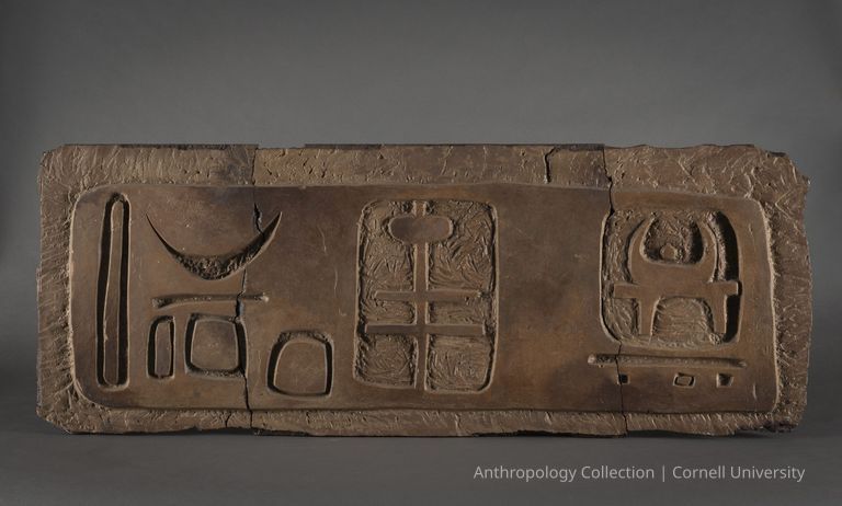 VOTIVE OF STILT-WALKERS | circa 1961-65 | Photo by Ann Cady, 2024 | ©2026 Norman Daly Art — A tripartite ancient stone tablet featuring intricate, deeply carved symbolic images. The overall texture is rough and its rustic appearance suggests the religious significance of the carvings displayed.