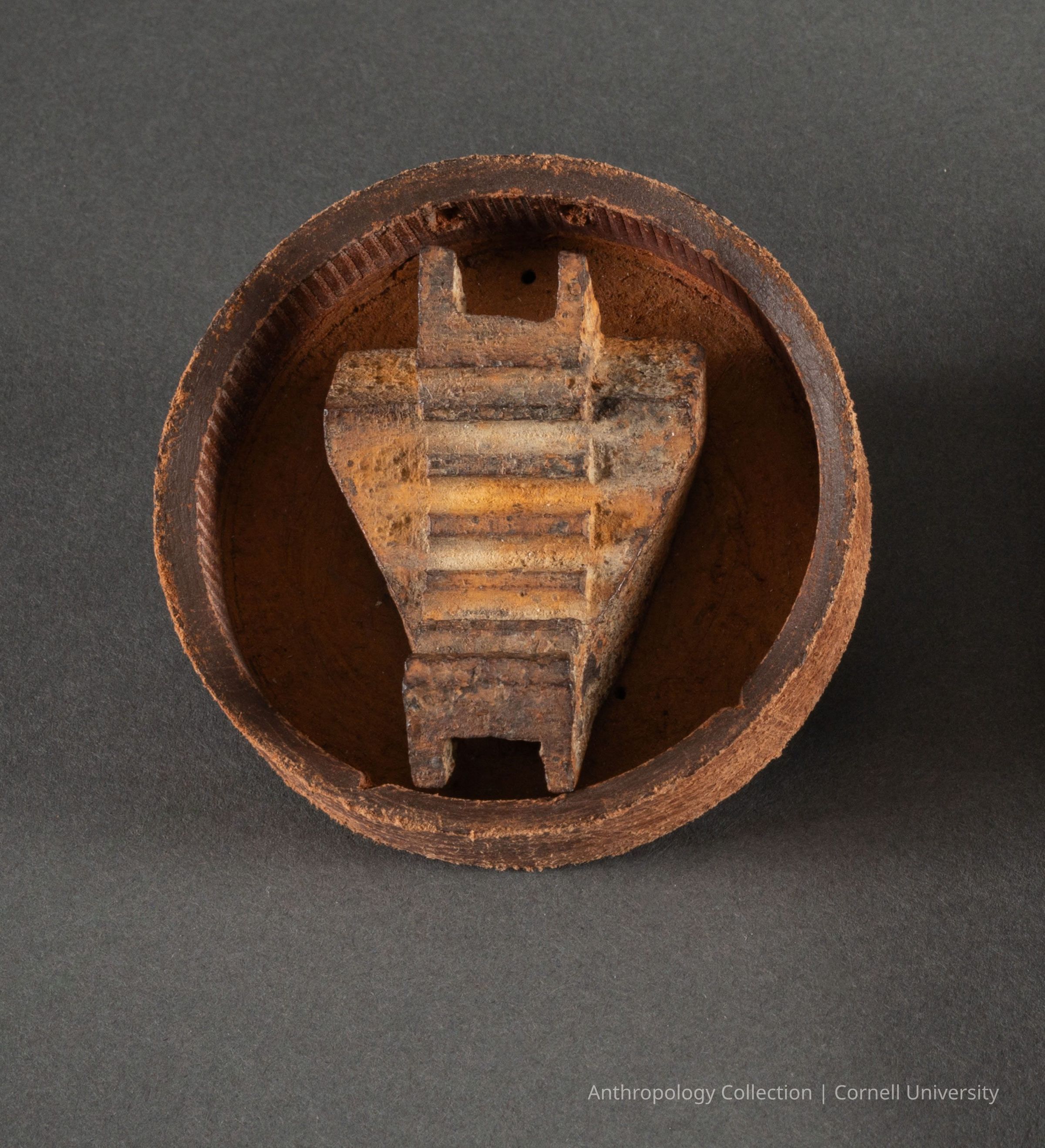 UNIVELL (Oil Applicator) | circa 1966-71 | Photo by Ann Cady, 2024 | ©2026 Norman Daly Art: A circular, rusted metal object with a rough texture displays a central, triangular component featuring parallel, horizontal ridges and a small open slot at the base, all revealing signs of significant weathering and age, suggesting it is an antiquated artifact, possibly used in to serve a specific functional purpose, highlighting the effects of time and exposure to the elements.