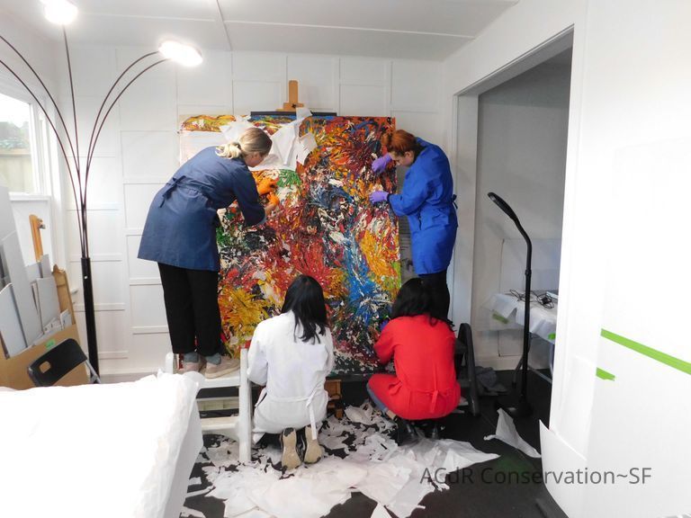Fabiola, Elle, Abby, and Tanya removing the paper from the face of the painting. Used scissors to cut around areas that were attached to the paint itself and pulled off unattached pieces. 