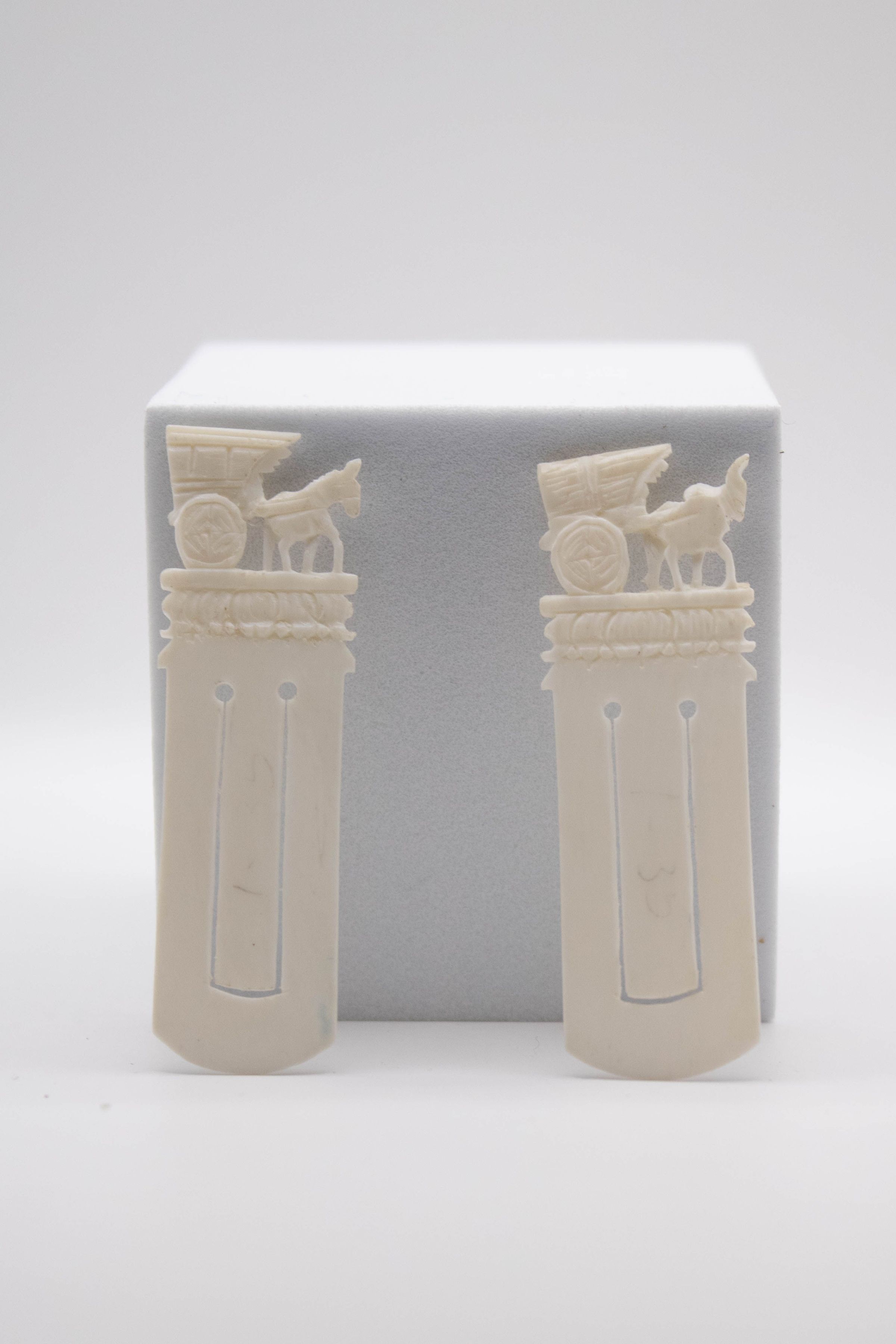 Set of two carved ivory bookmarks with a burro and cart.: Image of the set of two carved ivory bookmarks with a burro and cart on the top. The one on the left shows a cart used for the transportation of people while the one on the right shows one used for moving hay. The one on the right is also chipped on the front of the burro.