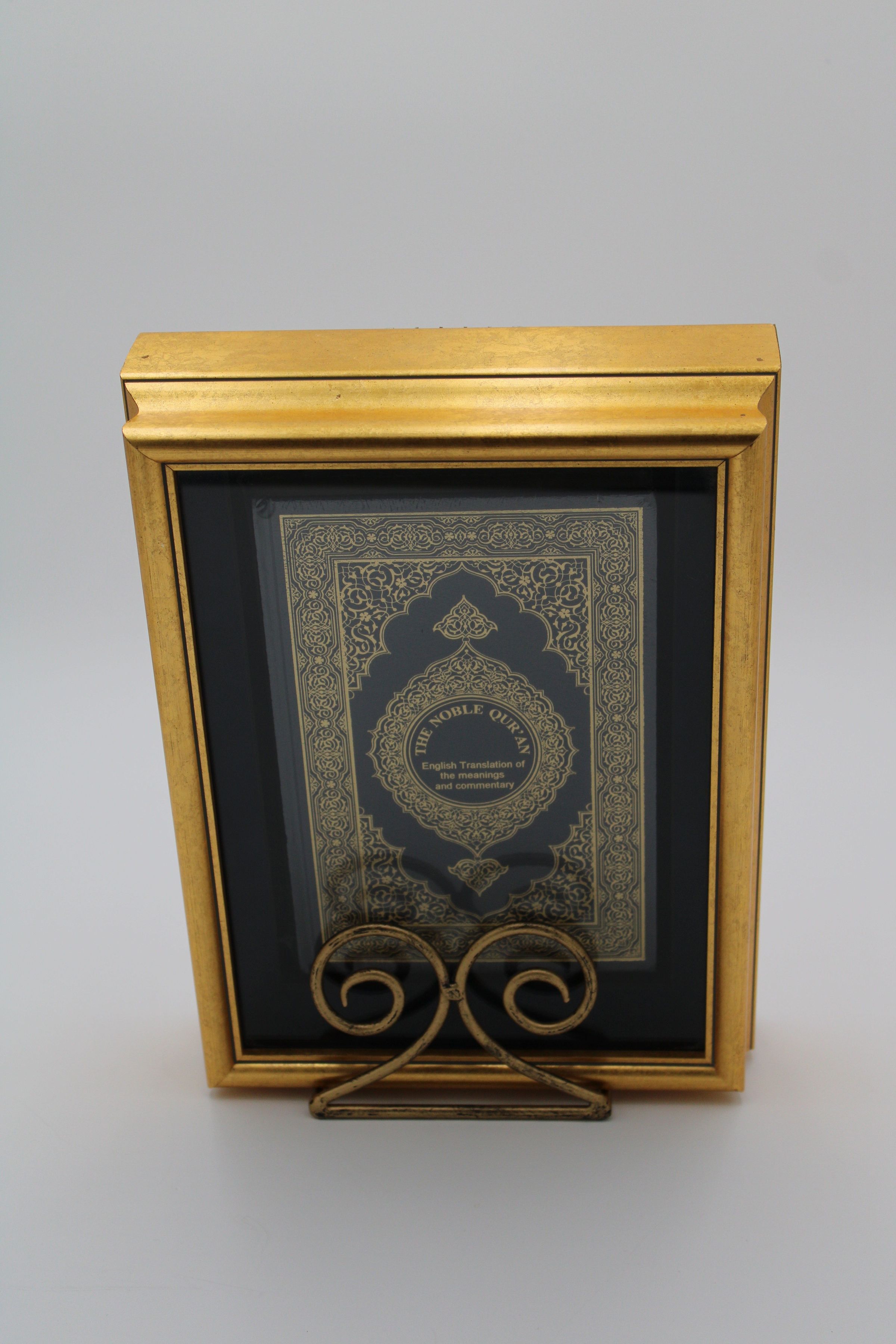 Front of “The Noble Quran”: The Front of "The Noble Quran" features a yellow Islamic ornamental design on black leather. In the middle is a circle with the title and subtitle of "Interpretation of the Meanings of the Noble Qur'an in the English Language" in English. It is in a large golden case with a glass front, and has a gold stand.